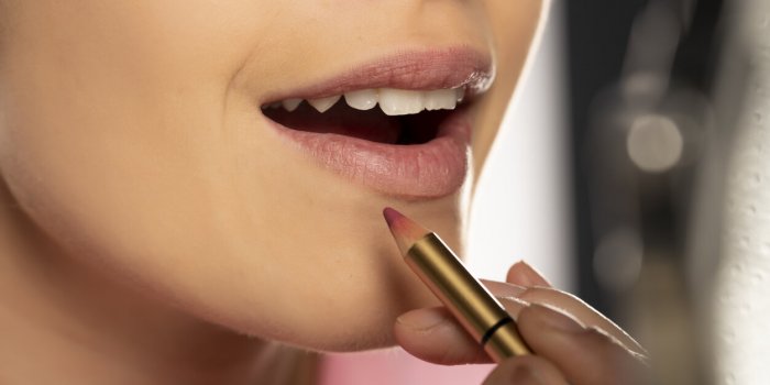 young woman applying lip pencil on her lips on white background