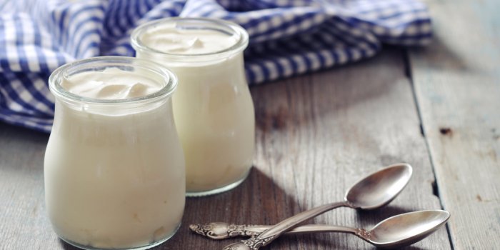 greek yogurt in a glass jars with spoons on wooden background