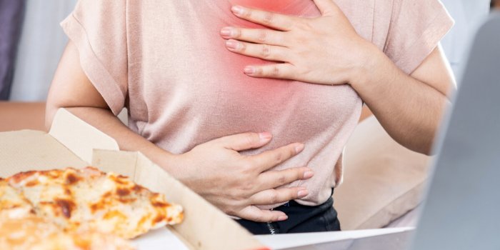 woman suffering from chest pain , heartburn caused by acid reflux after eating junk food pizza