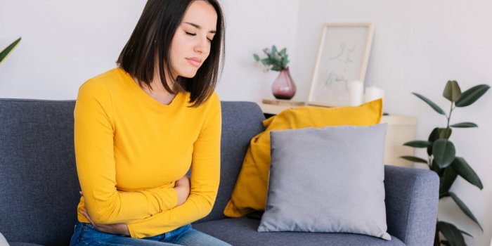 young woman suffering stomach ache or abdominal pain while sitting on couch at home menstruation or pregnancy health care...