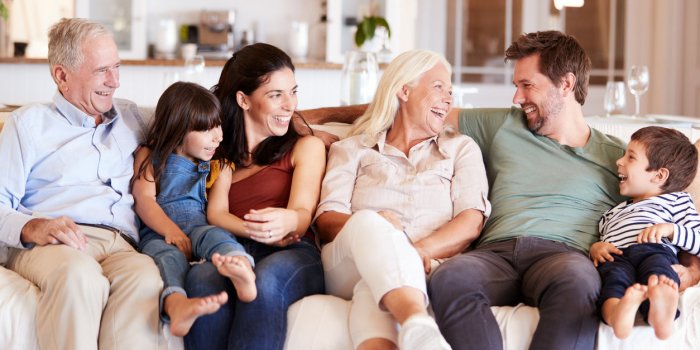 happy three generation white family sitting on a sofa at home looking at each other, front view