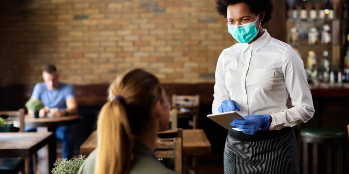 happy black waitress wearing protective face mask while taking order from customer on a touchpad in a cafe