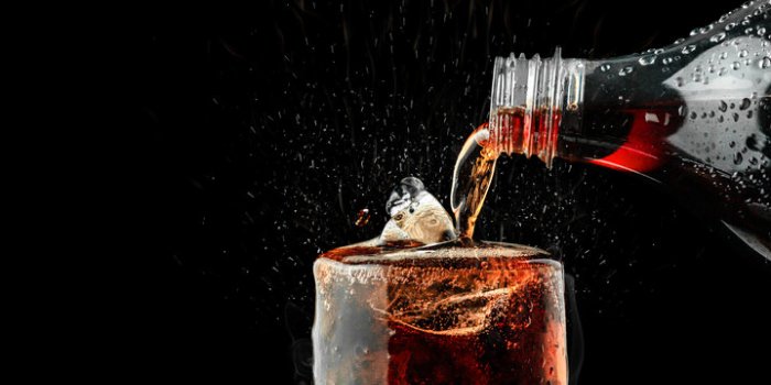 pour soft drink in glass with ice splash on dark background
