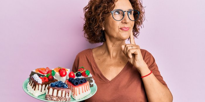 beautiful middle age mature woman holding cake slices serious face thinking about question with hand on chin, thoughtful ...