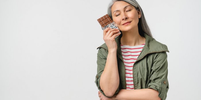 dreamy caucasian mature middle-aged woman with grey hair in casual clothes wants to eat chocolate bar full of calories is...