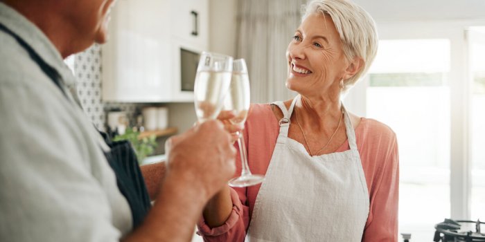 senior couple, champagne and drinks toast in house or home kitchen in marriage anniversary, celebration event or retireme...