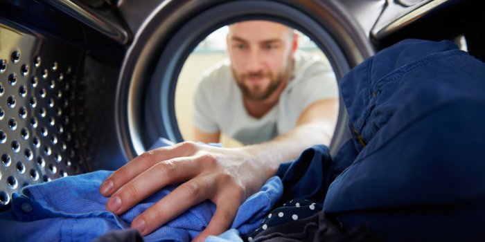 man doing laundry reaching inside washing machine