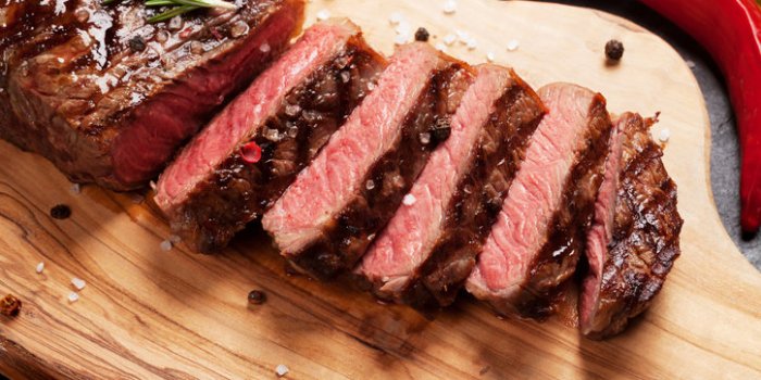 grilled striploin sliced steak on cutting board over stone table