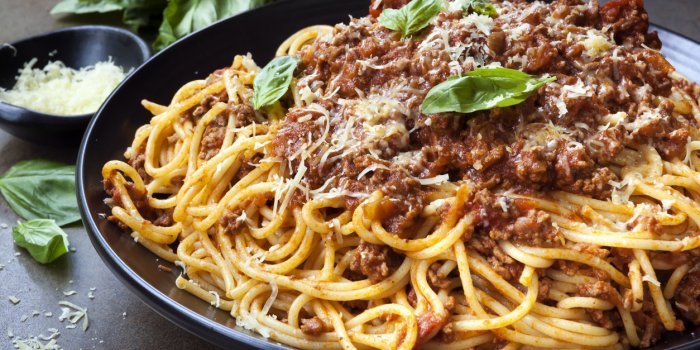 spaghetti bolognese in black serving platter, with fresh basil and parmesan