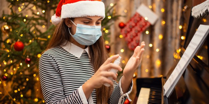 cheerful girl in red santa hat and protective medical mask applying hand sanitizer to hands while playing the piano