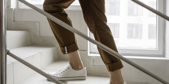 woman in white sneakers and khaki trousers goes upstairs to her apartment white staircase in apartment building casual ou...