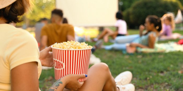 Young woman with popcorn watching movies in open air, close-up space for text