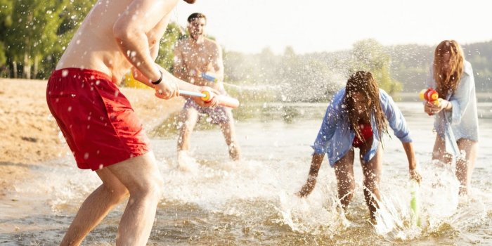 Happy friends fighting with water guns - youth, summer lifestyle and holiday ideas