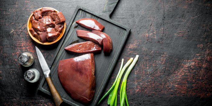 pieces of raw liver in a plate and on a cutting board on dark rustic background