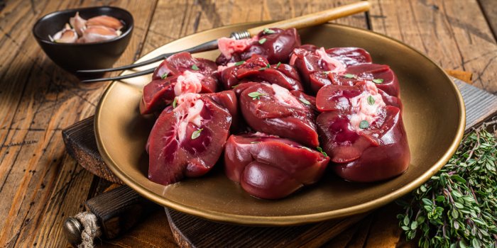 lamb kidney, raw sliced offal on plate with thyme wooden background top view