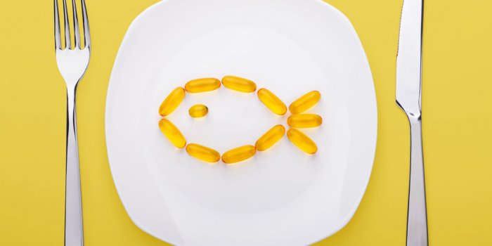 fish oil soft gels lying on white porcelain plate in the form of fish (yellow background)