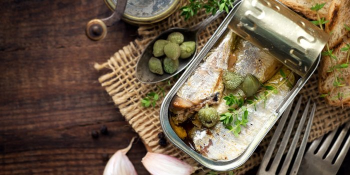 open tin of sardines in olive oil with capers and thyme on dark rustic wooden background