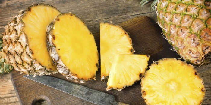 one whole and one sliced pineapples on wooden background