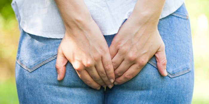 close up picture of a young woman holding her butt, she needs to poop, outdoor