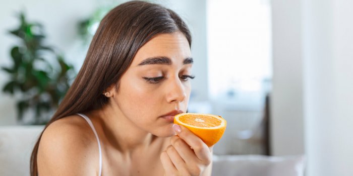 sick woman trying to sense smell of half fresh orange, has symptoms of covid-19, corona virus infection - loss of smell a...