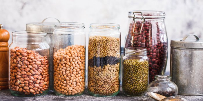 collection of grain products, lentils, peas, soybeans and red beans in storage jars over on kitchen rural table vegetaria...