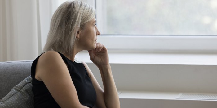 thoughtful depressed mature woman sitting on couch at home, looking at window away in deep thoughts, suffering from depre...