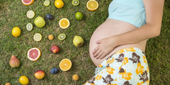 pregnant woman is laying on grass with fruit