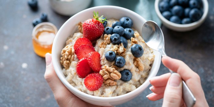 oatmeal porridge bowl with berry fruits in female hands, closeup view healthy vegetarian breakfast food