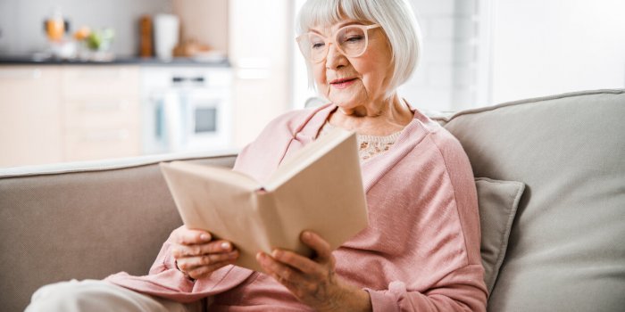 old lady sitting on couch and enjoying interesting novel stock photo