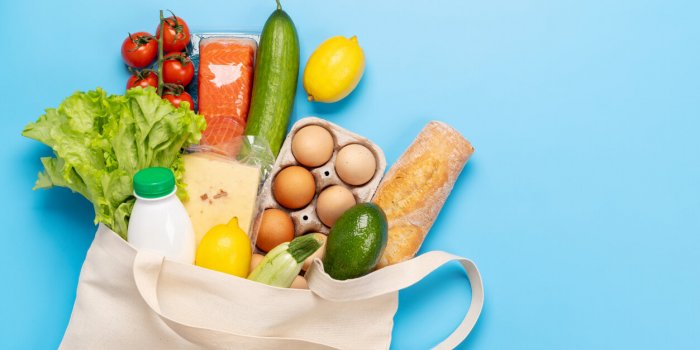 shopping bag full of healthy food on blue background flat lay with copy space