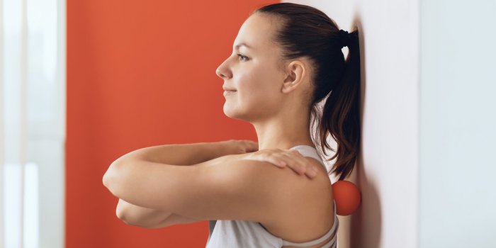 beautiful woman performs myofascial release of hyper-flexible muscles of the back with a massage ball near the wall the c...