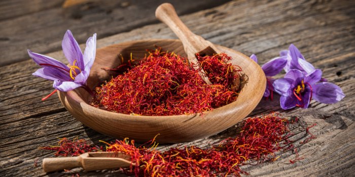 saffron in wooden bowl on wooden table with saffron flowers on the side