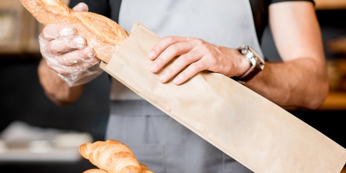 seller packing bread into the paper bag in the bakery shop, close-up view on the bag with copy space