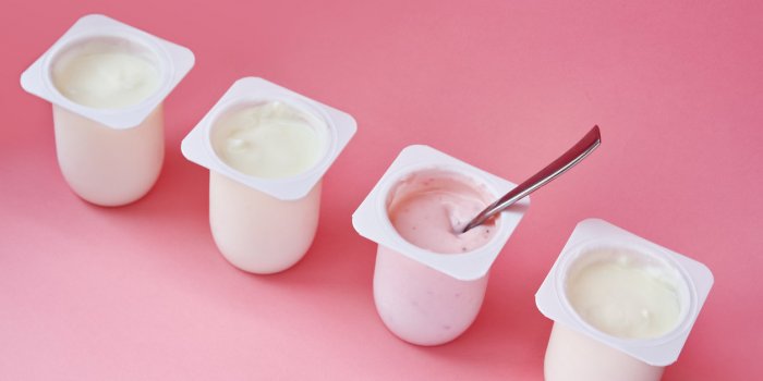 four yogurts in white plastic cups on pink background with copy space strawberry pink yoghurt with spoon in it minimal st...