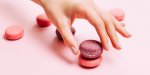 beautiful female hands with trendy manicure holding pink macaroon cake top view, flat lay copyspace for your text