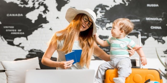 happy and playful woman with baby boy sitting at the travel agency office with beautiful map on the background ready for ...