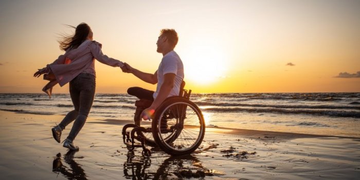 handicapped man in wheelchair and his girlfriend on a beach at sunset