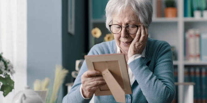 sad senior woman mourning the loss of her husband, she is holding a picture and crying