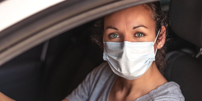 young woman driving car with protective mask on her face covid-19 coronavirus healthcare or allergy protection
