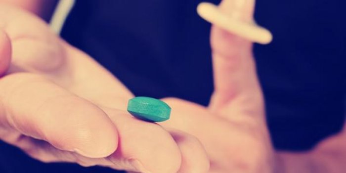 gros plan d'un jeune homme avec une pilule bleue dans une main et un préservatif dans l'autre main, avec un effet de filtre