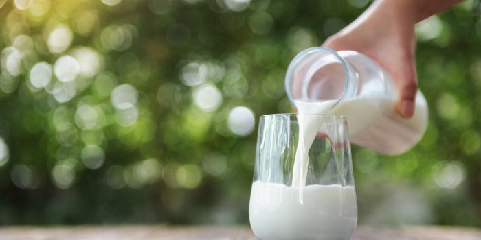 pouring milk in the glass on the wooden table with bokeh background of nature