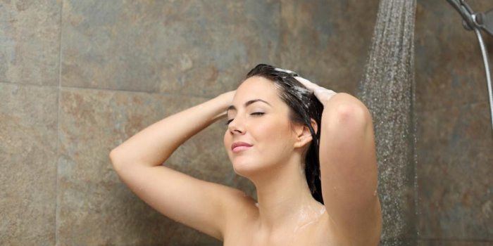 femme détendue douche nettoyant ses cheveux avec du savon dans la douche sous un jet d'eau
