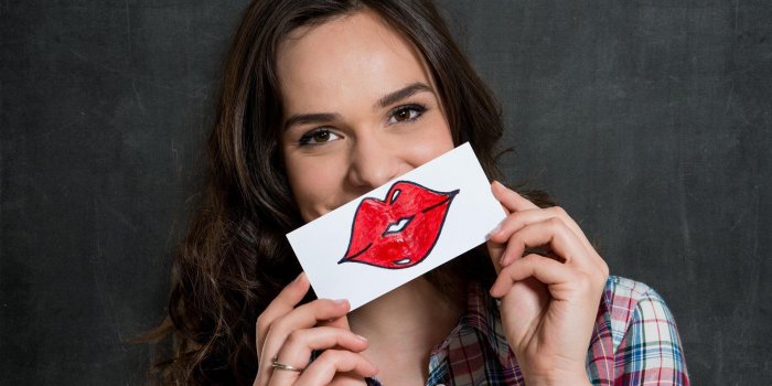 belle fille tenant une feuille de papier avec des lèvres rouges dessinés isolé sur fond gris