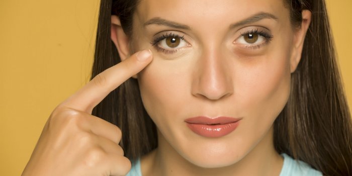 young woman applying concealer on her low eyelids on yellow background
