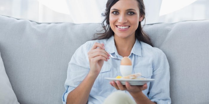 cheerful brunette eating eggs in her living room