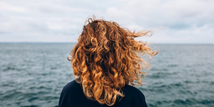 view from the back a woman with curly hair looks at the sea