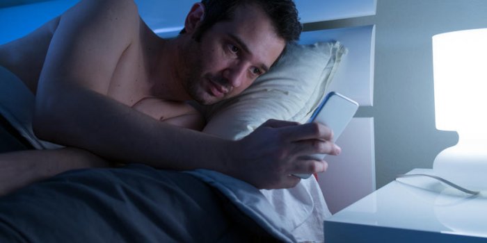 homme au lit avec un téléphone portable à la main