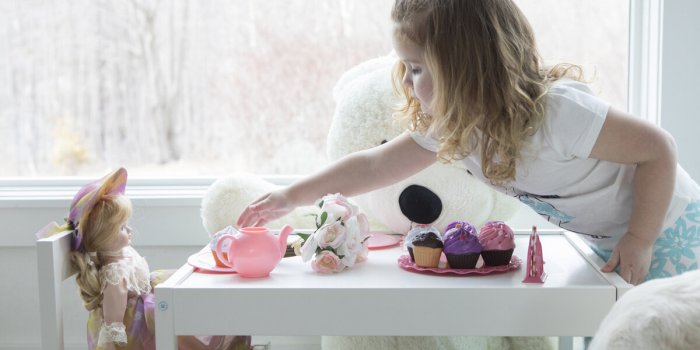 a little girl has a tea party with her doll and dog