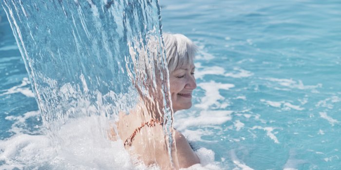 senior caucasian smiling woman with gray hair enjoying falling on her shoulders flow of water hydromassage in outdoor the...