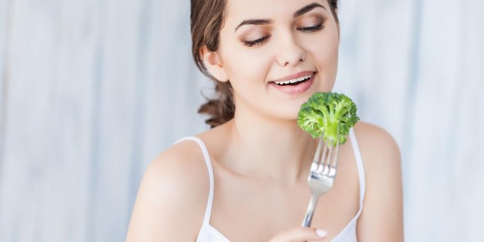portrait of happy smiling young beautiful woman eating broccoli